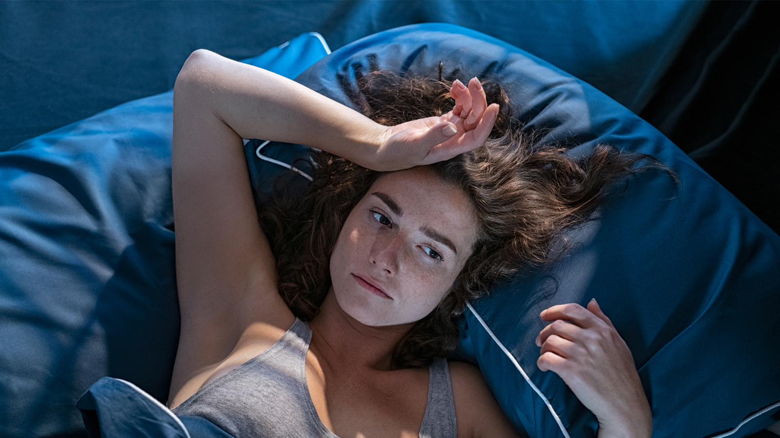 Une femme fatiguée est allongée dans son lit, épuisée par un sommeil agité en raison de la chaleur.