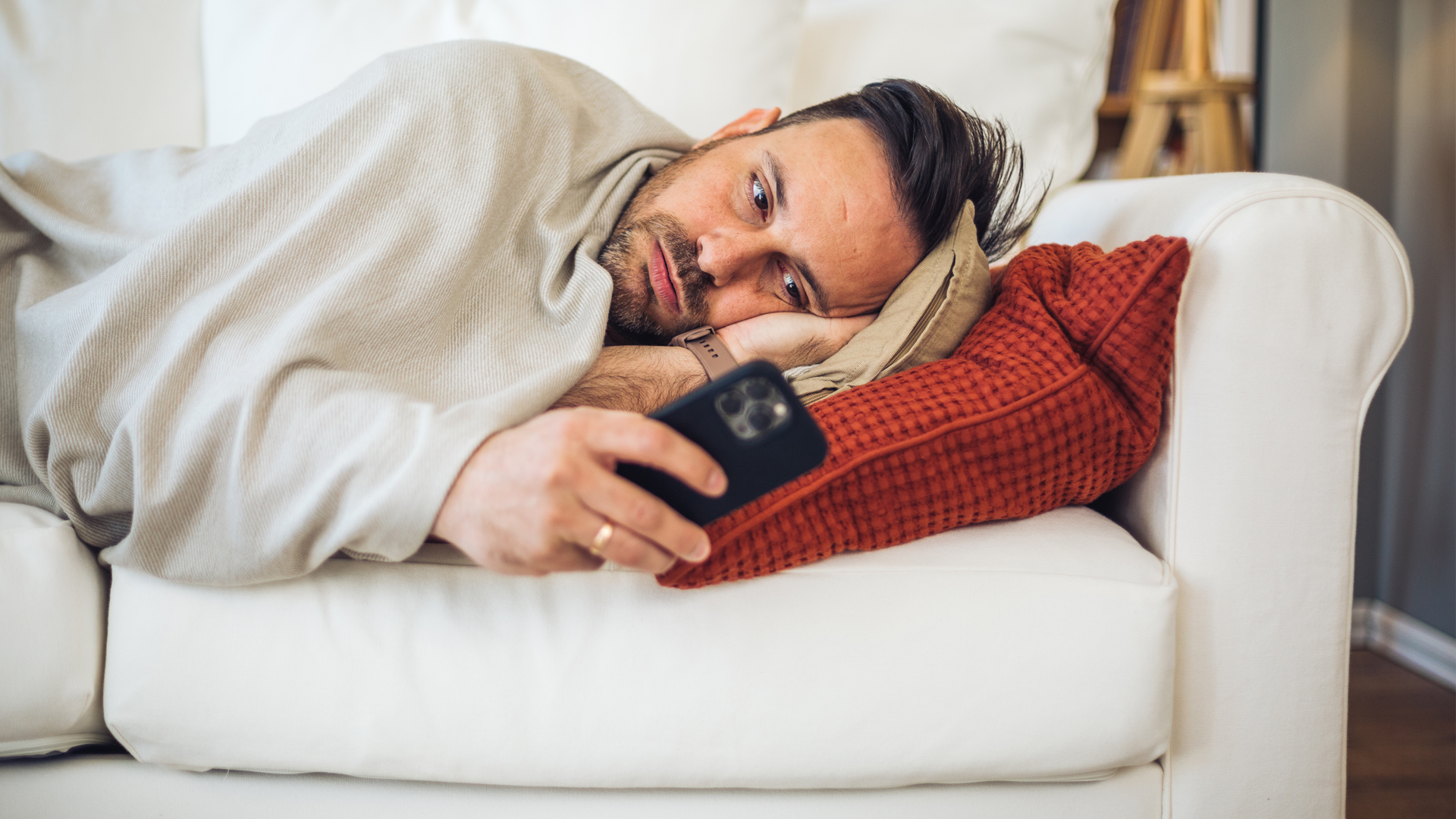 Mann liegt im Bett und nutzt sein Smartphone, um seine Symptome online zu checken.