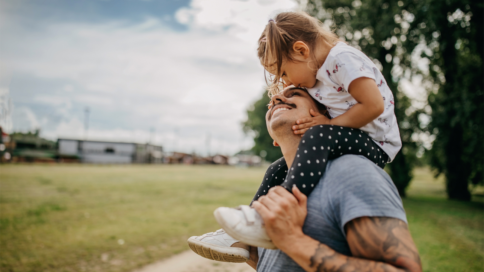 A father carries his daughter on his shoulders, smiling at having found the perfect health insurance for children.