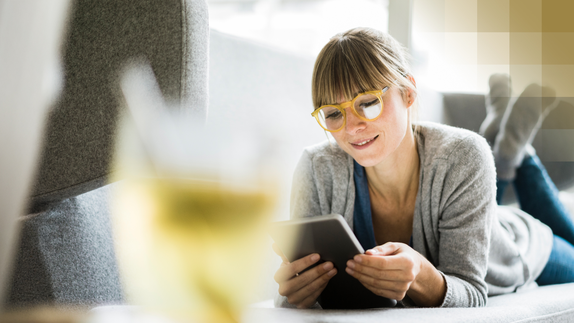 Une femme est allongée sur un canapé und lit des articles sur la santé sur une tablette dans le guide de la KPT « recevoir des connaissances ».