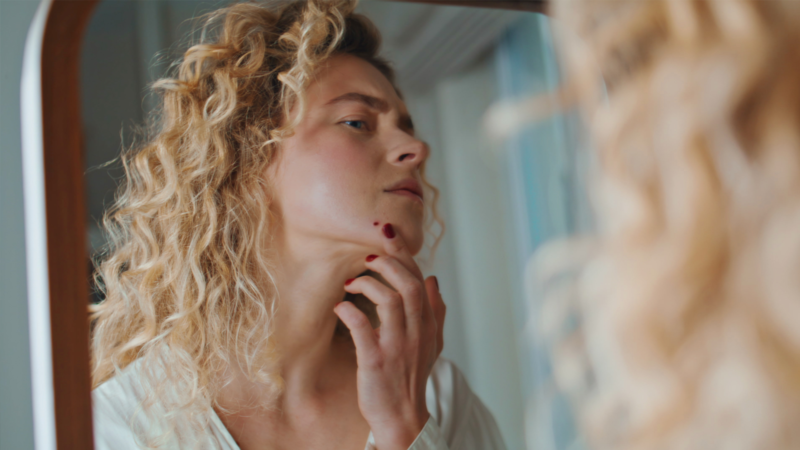Une femme s'examine dans le miroir et contrôle attentivement un grain pour la prévention du cancer de la peau.