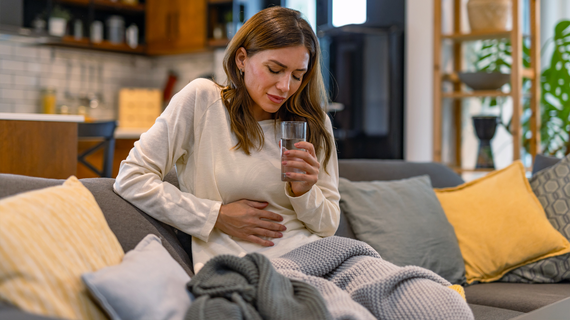 Femme atteinte de gastro-entérite assise sur un canapé avec un verre d’eau