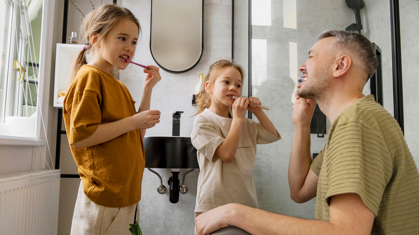 Un père montre aux enfants dans la salle de bain comment bien se brosser les dents.