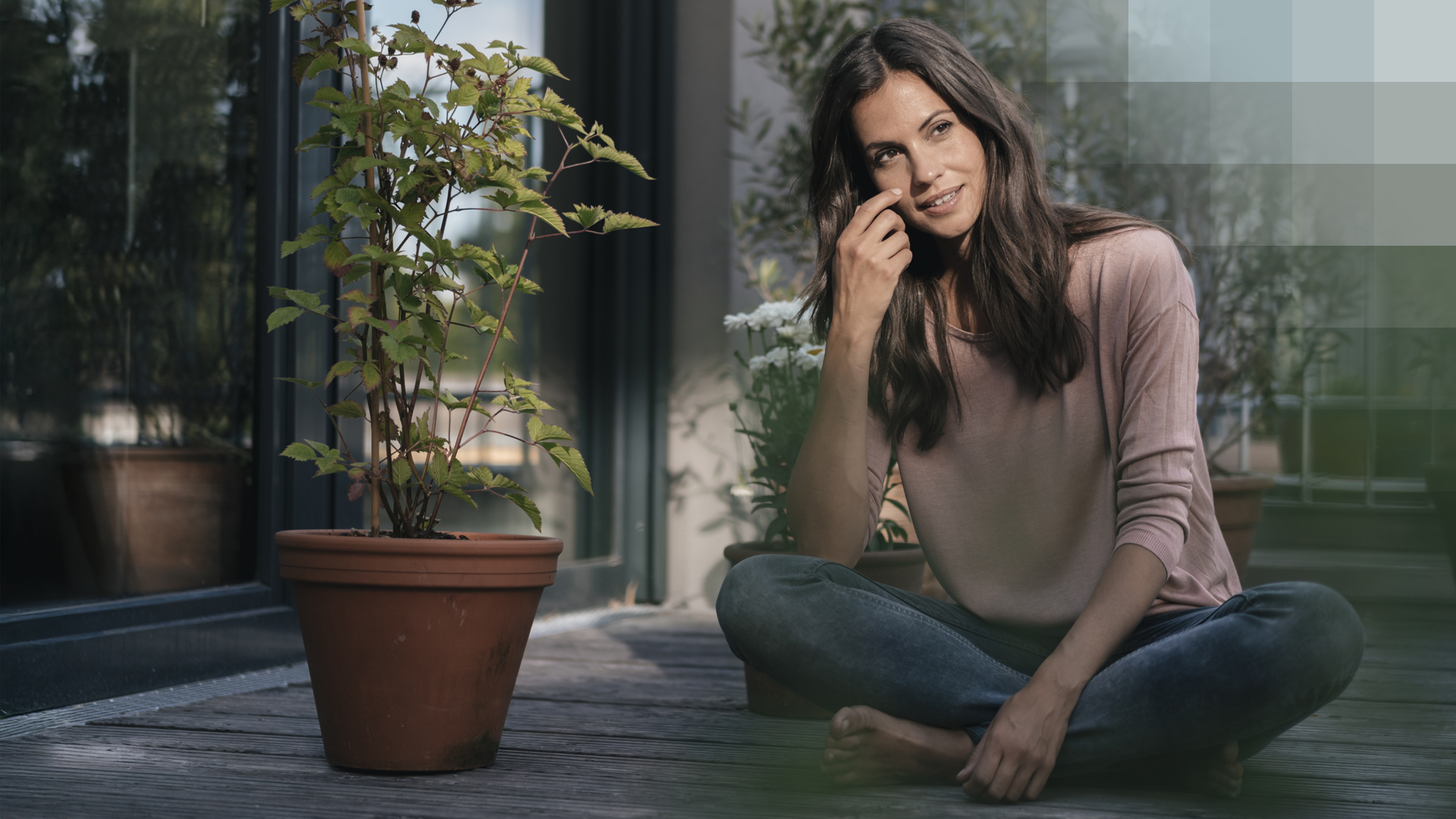 Une jeune femme est assise par terre sur son balcon, entourée de plantes, et réfléchit à son assurance ambulatoire.
